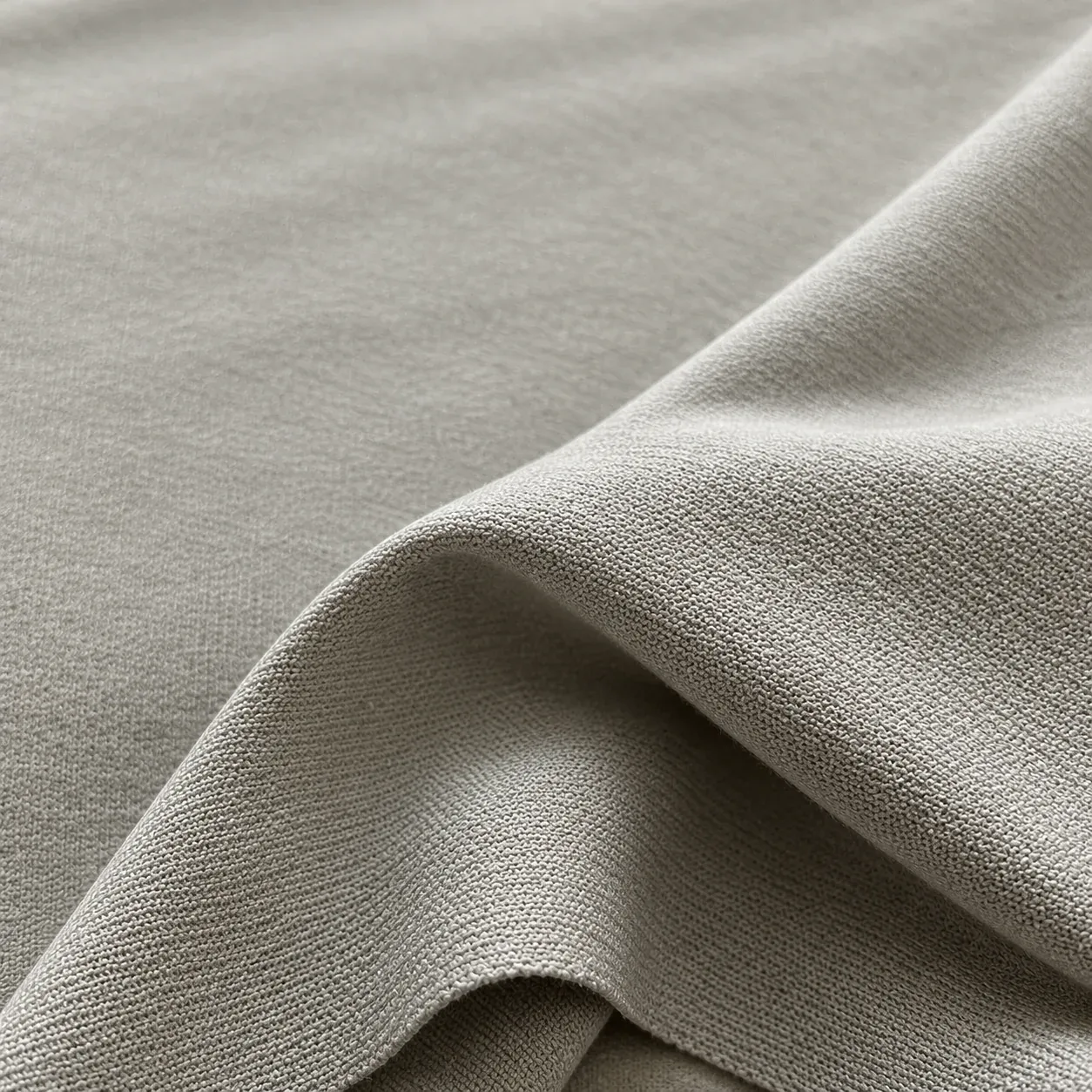 A close fold of fine greige Suvin cotton knit, showing the weave